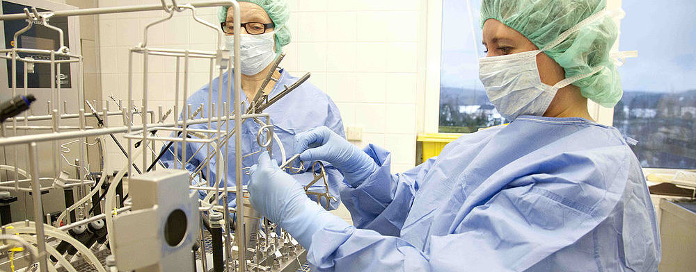 Zwei medizinische Fachkräfte in Schutzkleidung und Masken bedienen sterile Geräte in einem Labor mit Fensterblick